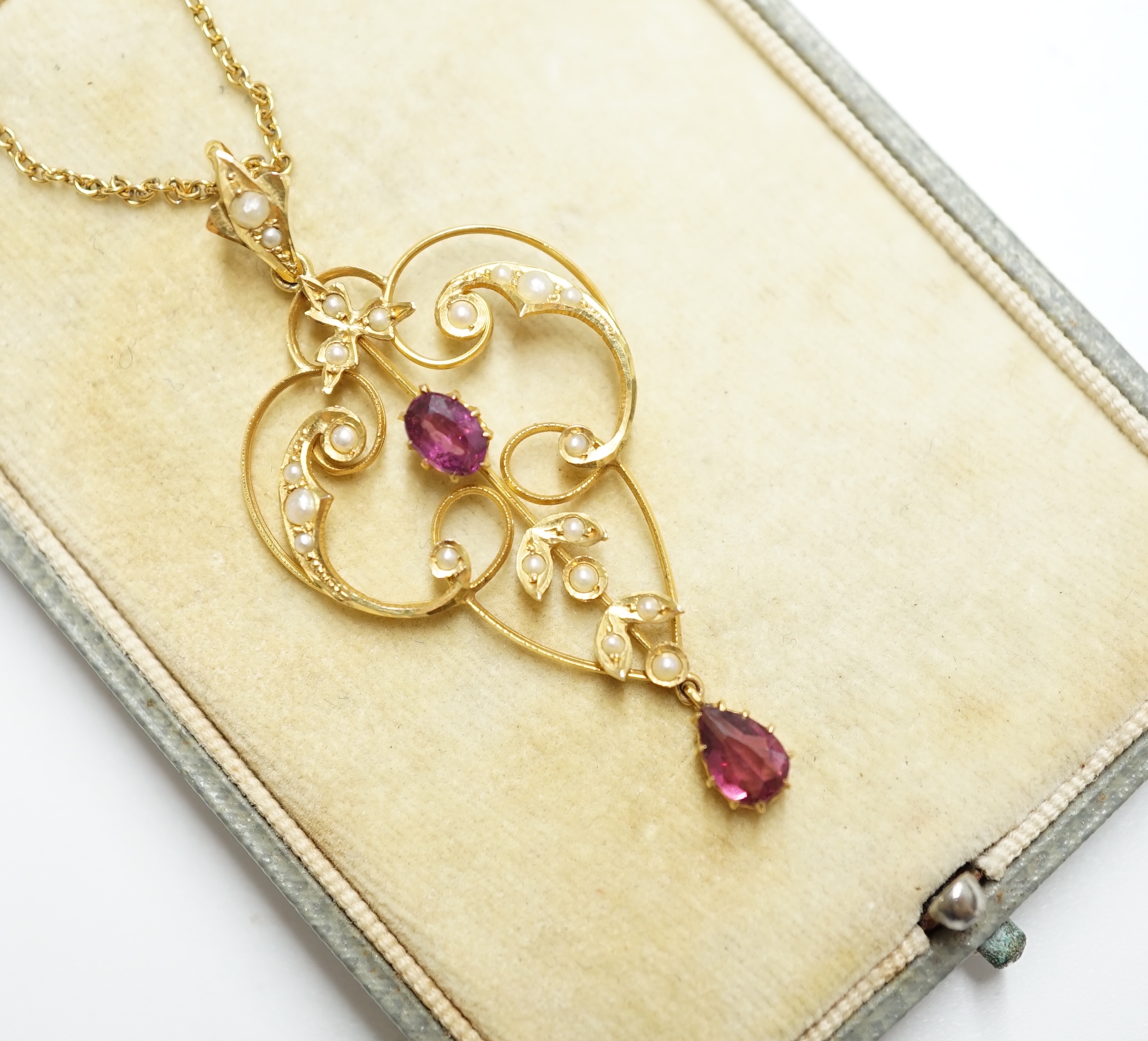 A cased Edwardian 9ct, garnet and seed pearl cluster set drop pendant, 52mm, on a yellow metal fine link chain, 40cm, gross weight 4.7 grams. Condition - fair to good